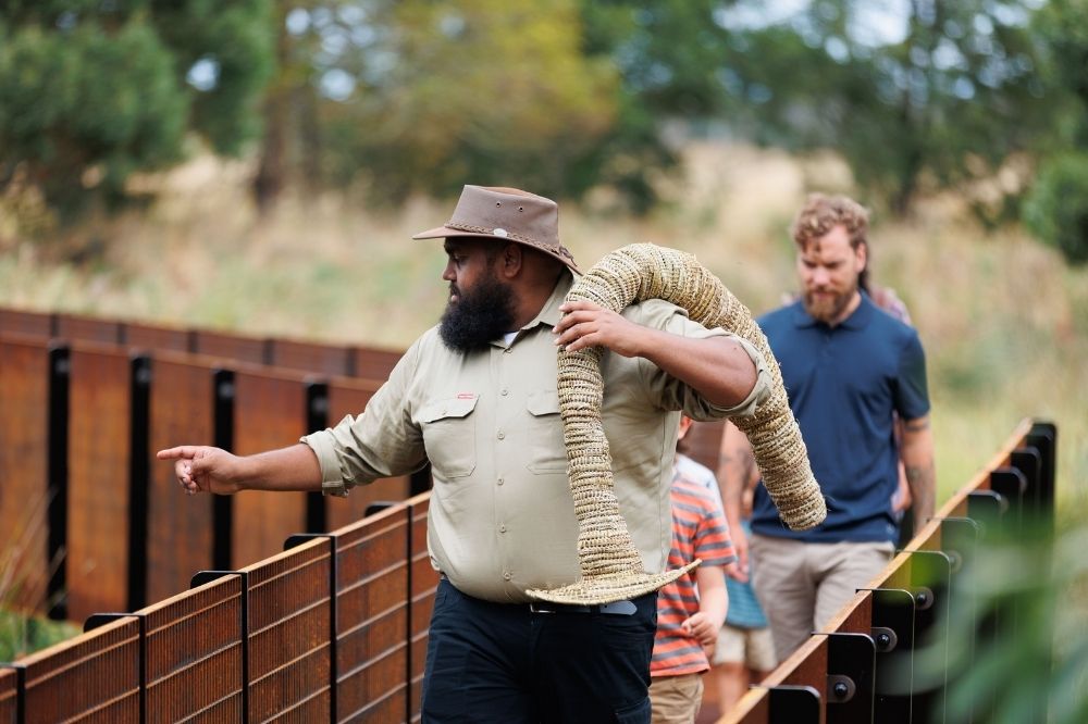 A tour guide carrying a woven object points out something in the reeds.