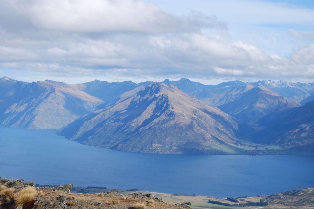 A panoramic view of mountains, some with snow caps, surrounded by a vast blue lake.