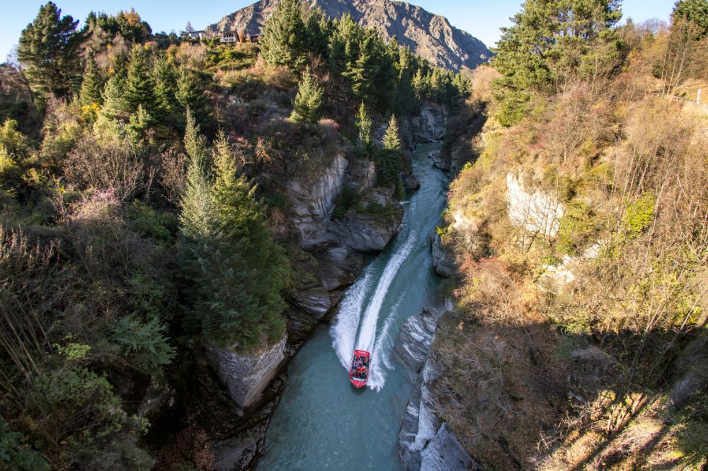 A red boat speeds down a narrow river with high rocks on either side.