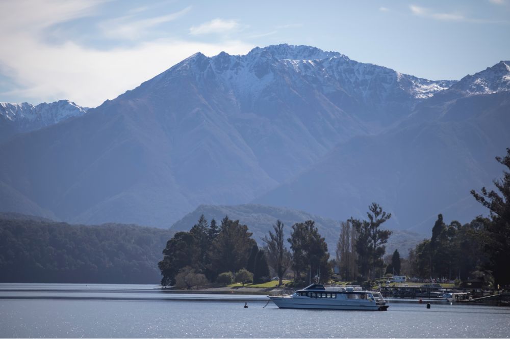 A large lake with snow capped mountains in the background .A boat floats in the still water.