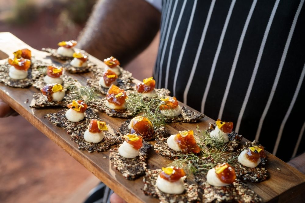A person holds a wooden tray of native Australian food.
