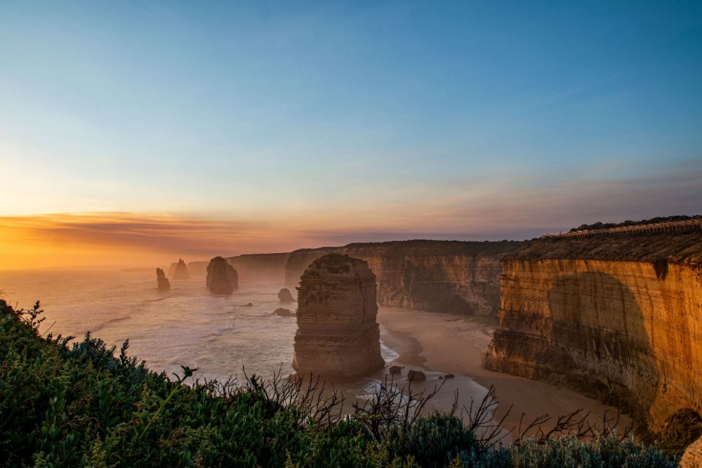 The twelve apostles sitting in the ocean with rolling waves. The sun sets with vibrant orange and purple colours