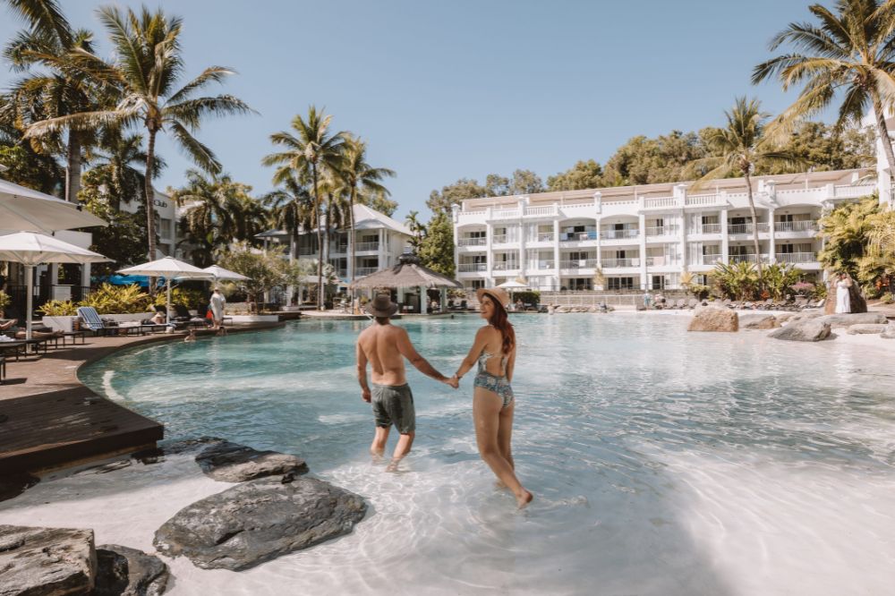 People hold hands in the resort pool surrounded by palm trees