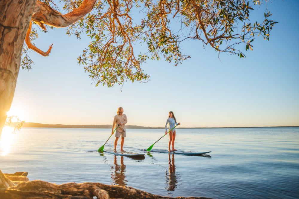 Two people on stand up paddle boards floating on calm blue water.