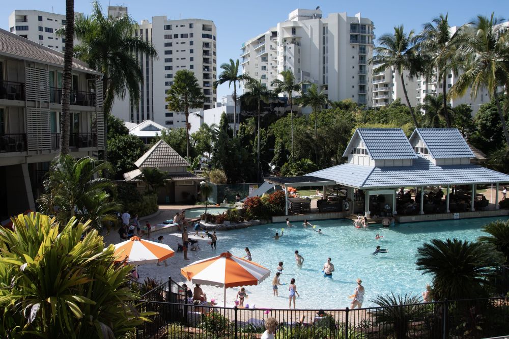 A resort pool with people enjoying themselves. The area is surrounded by palm trees