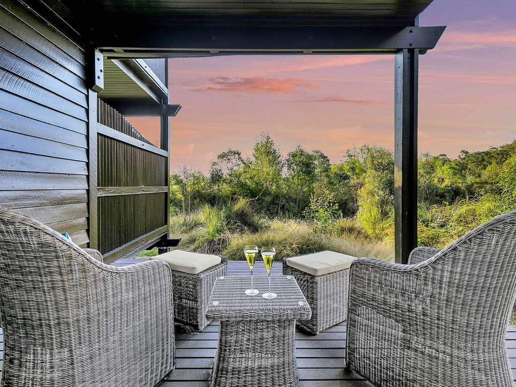 A secluded resort balcony with two glasses of champagne sitting on a table. The sun sets in purple and orange colours in the distance