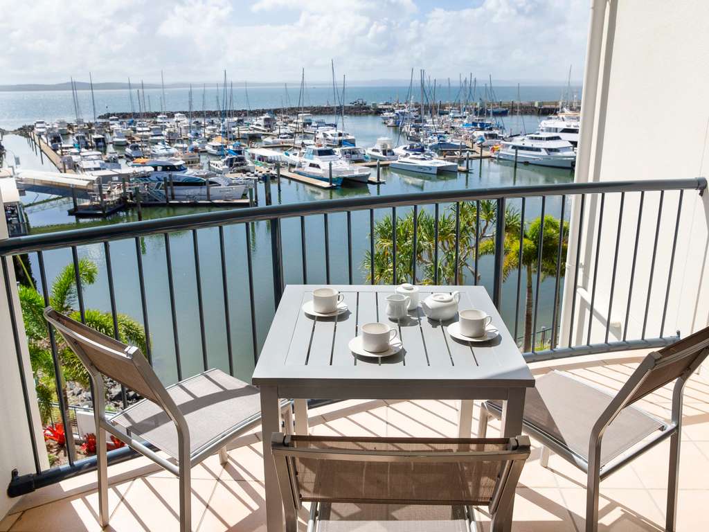 A hotel balcony with a table with tea cups. Overlooking a marina with boats in the harbour.