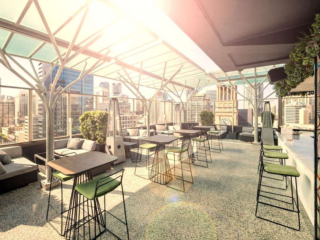 A hotel bar with lounge seats an high stools. The bar sits high on the rooftop with towering buildings surrounding