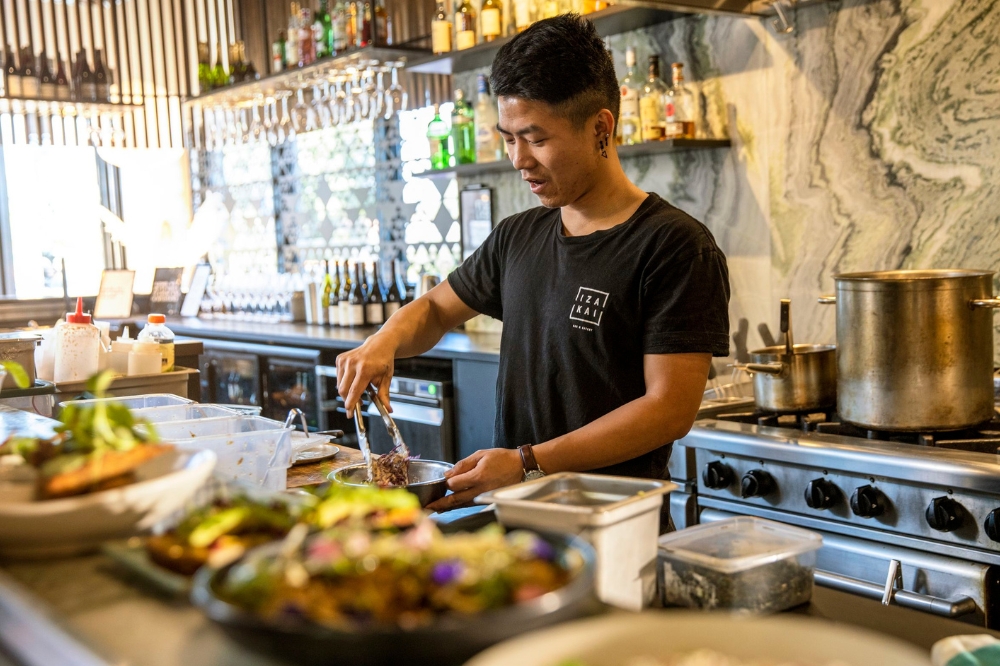 A person stands in a commercial kitchen plating up food