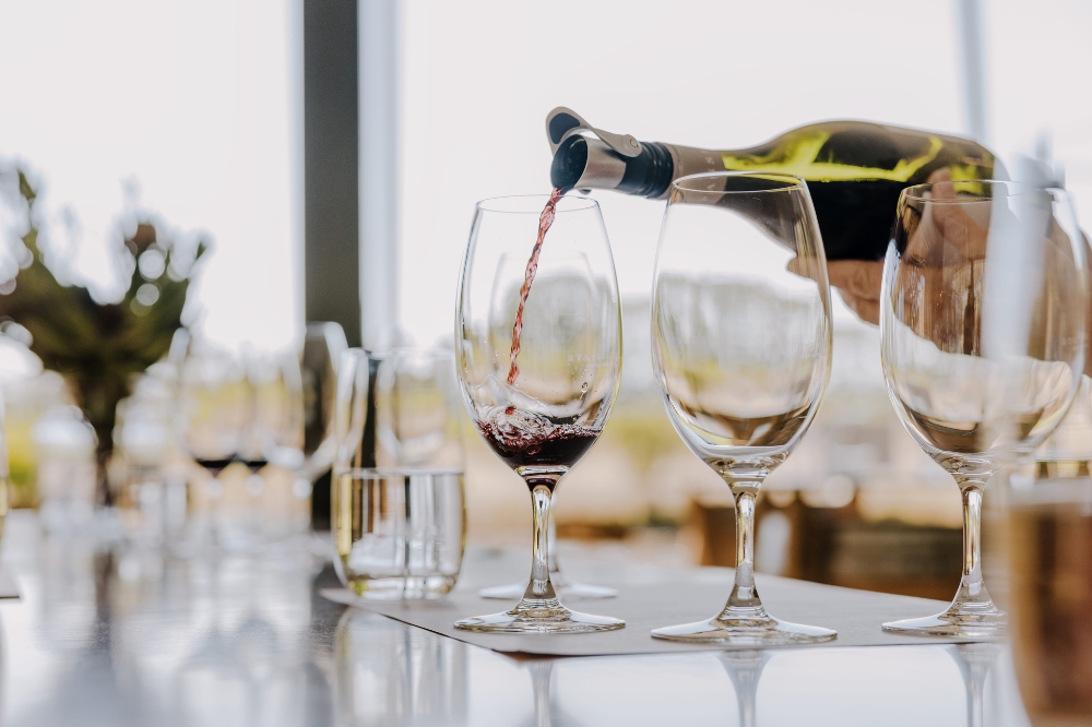 Three wine glasses on a table. Red wine is being poured into the far left glass