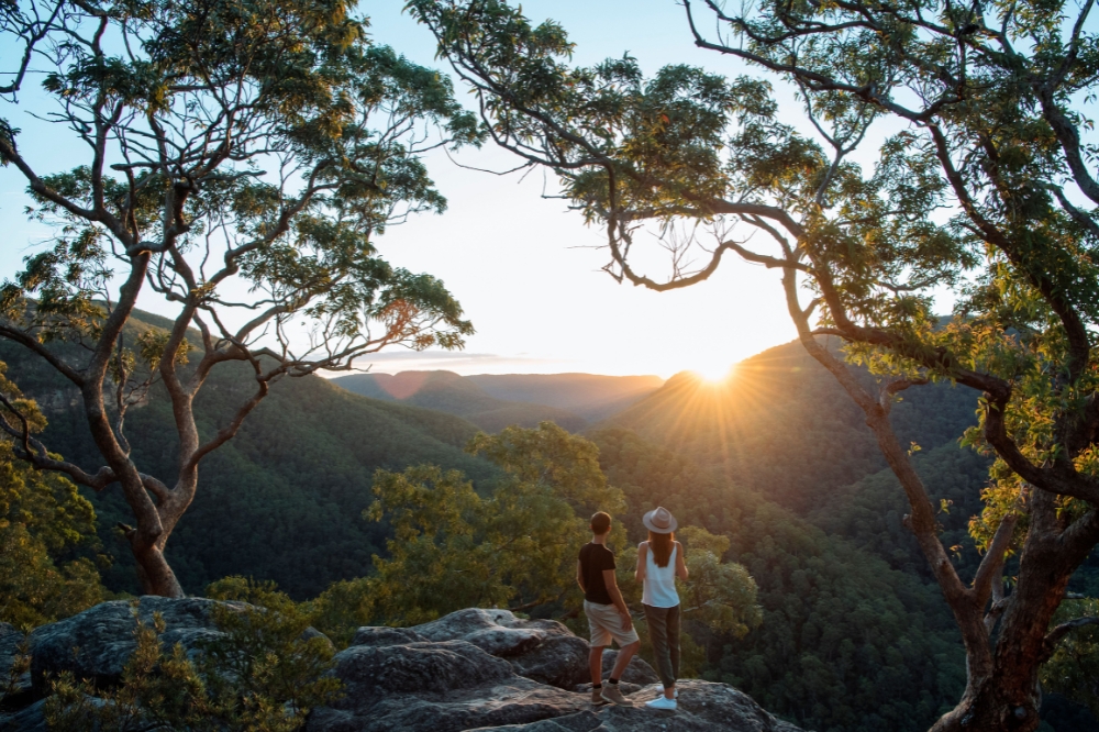 People stand on a rock overlooking surrounding mountains and trees