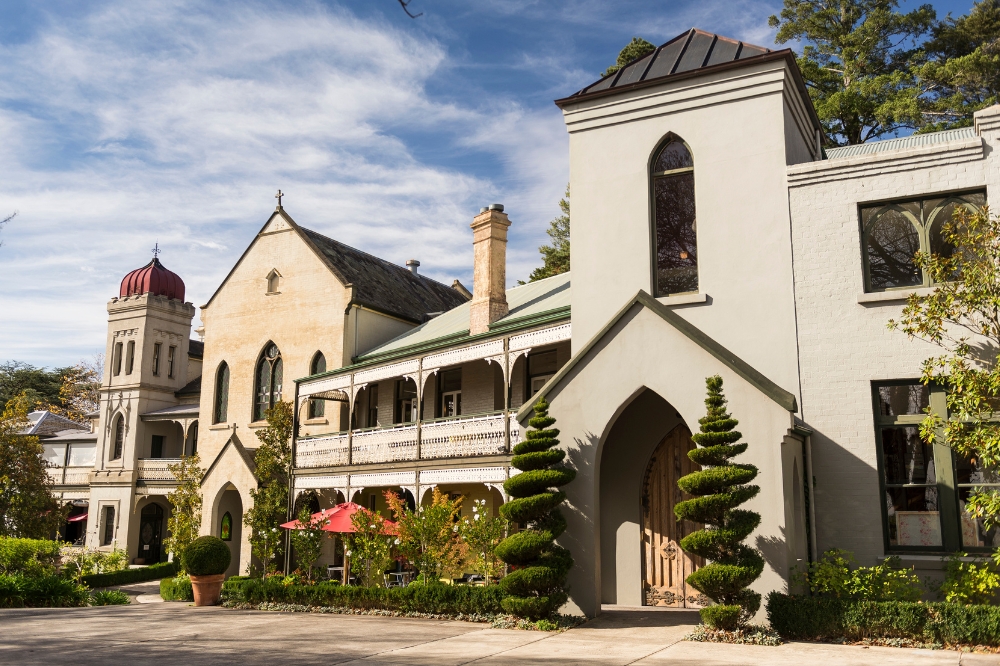 The outside of the Convent Daylesford. The gardens are surrounded by neat green hedges with flowers behind
