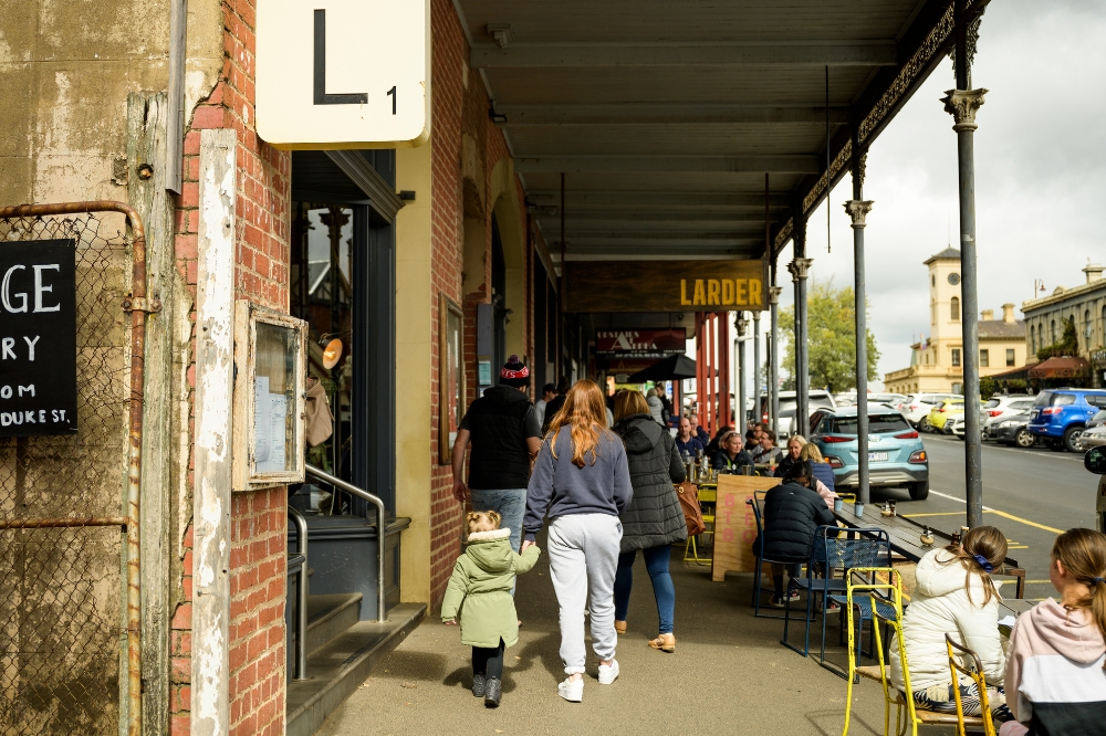 Groups of people walking along the street while people sit at cafes in outdoor tables.