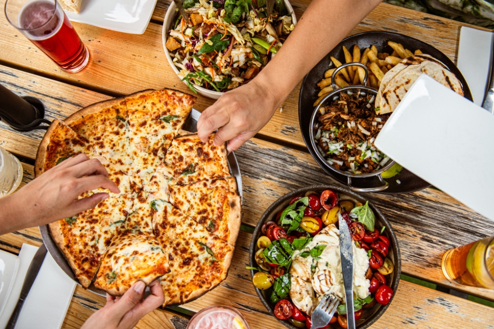 People's hands pick up food on a table with shared plates