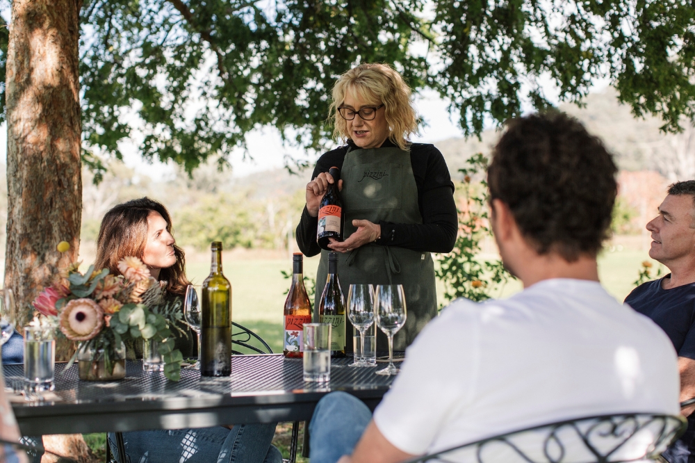 A person talking about the bottle of wine in their hands. The people at the table look at her with interest