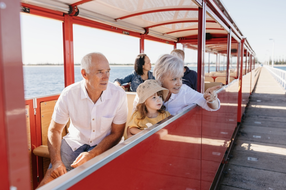 Two people hold a child pointing out of a red train window