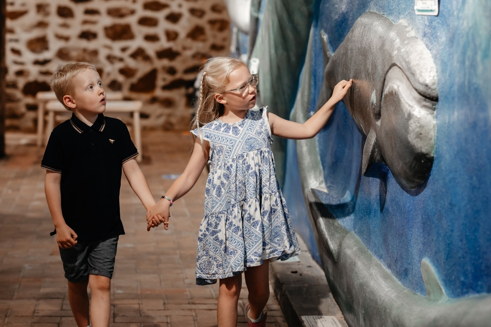 Two children walk hand in hand looking at diagram of a whale on a wall
