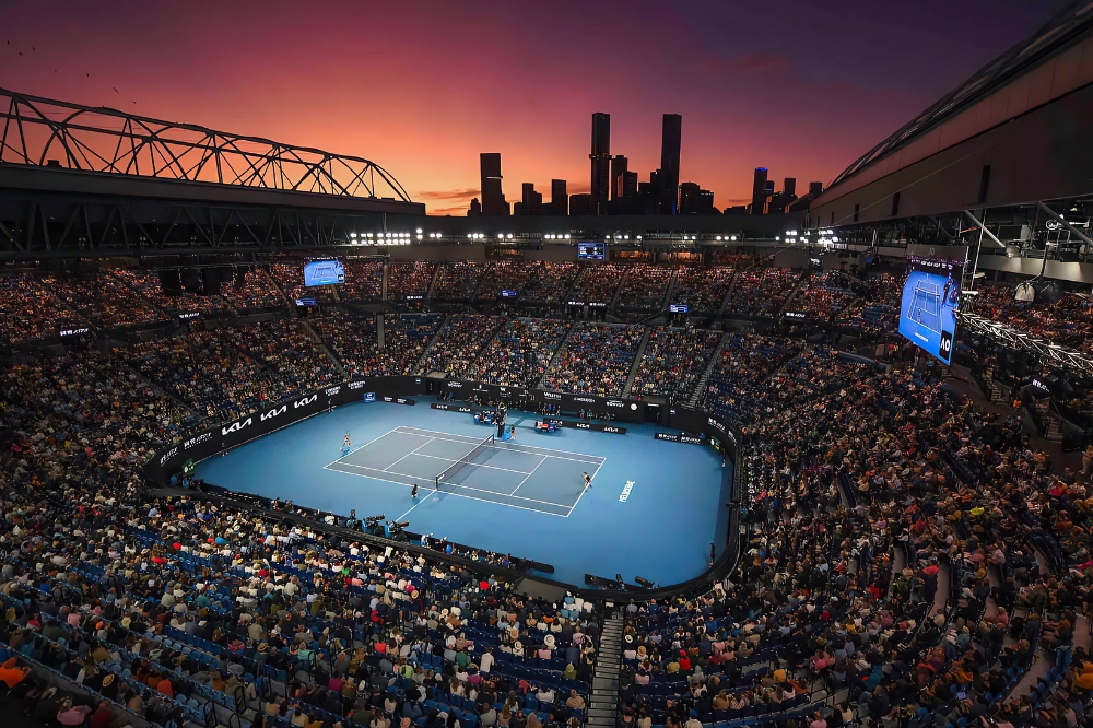 The sun sets with bright pink sky over a tennis court filled with spectators