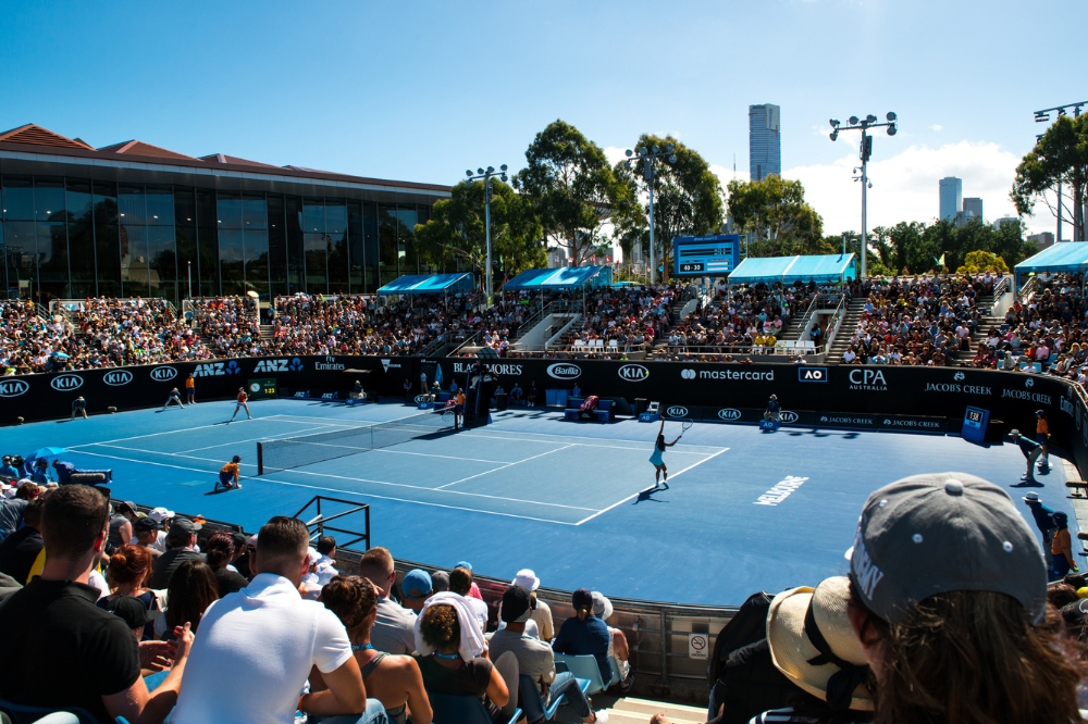 A large crowd watches a tennis match on a clear day