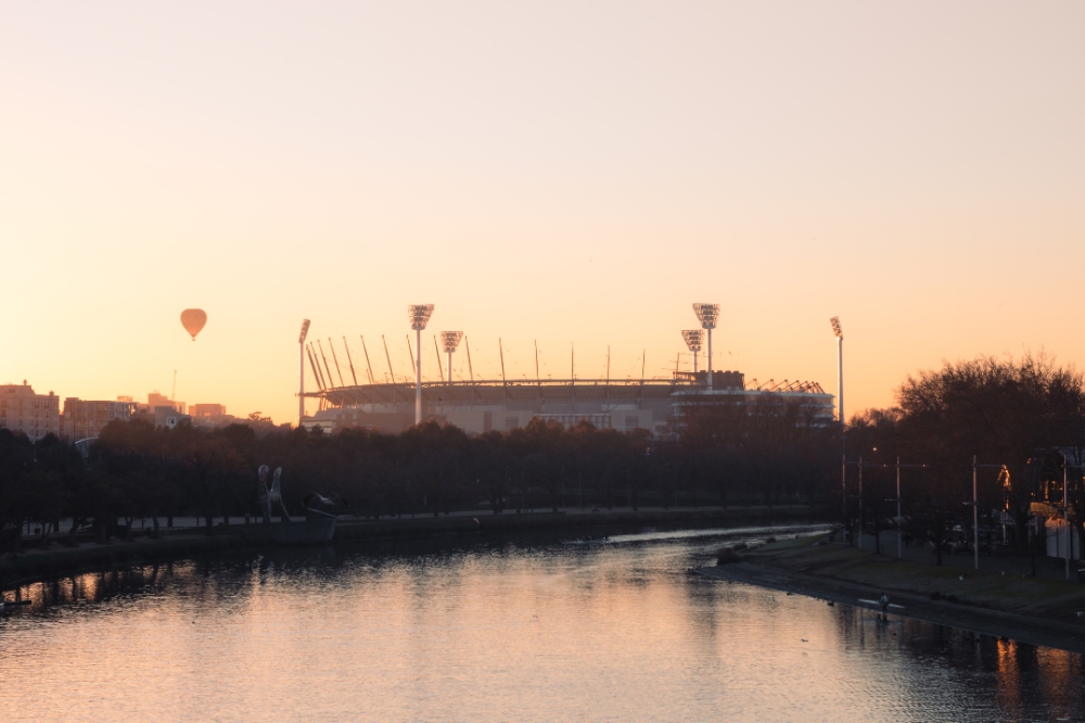 The Yarra river in the foreground the the MCG in the background with a hot air balloon in the sky