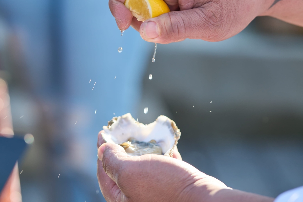A person squeezes lemon into a fresh oyster in their hand