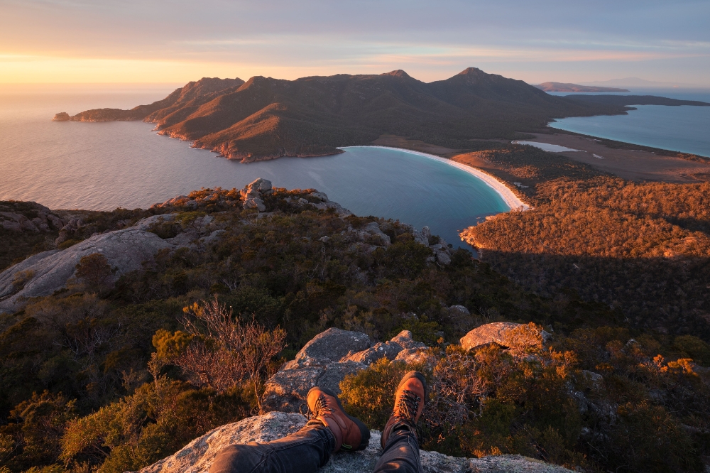 A lookout with a view of a clear blue bay with white sand surrounded by rocky hills and green trees