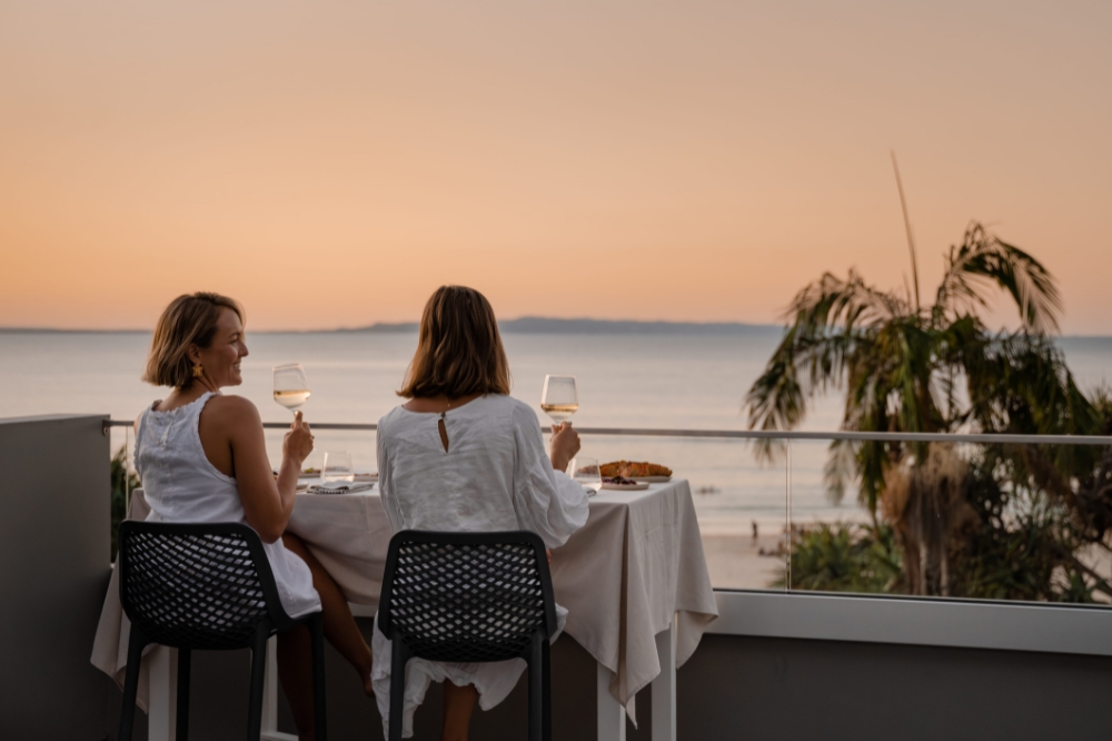 Two people enjoy dinner overlooking the beach at sunset