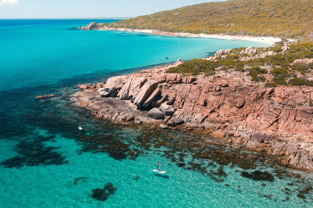 An aerial view of a person stand up paddle boarding in crystal clear blue water